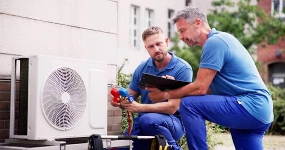 Two technicians reviewing HVAC system readings with gauges and a tablet